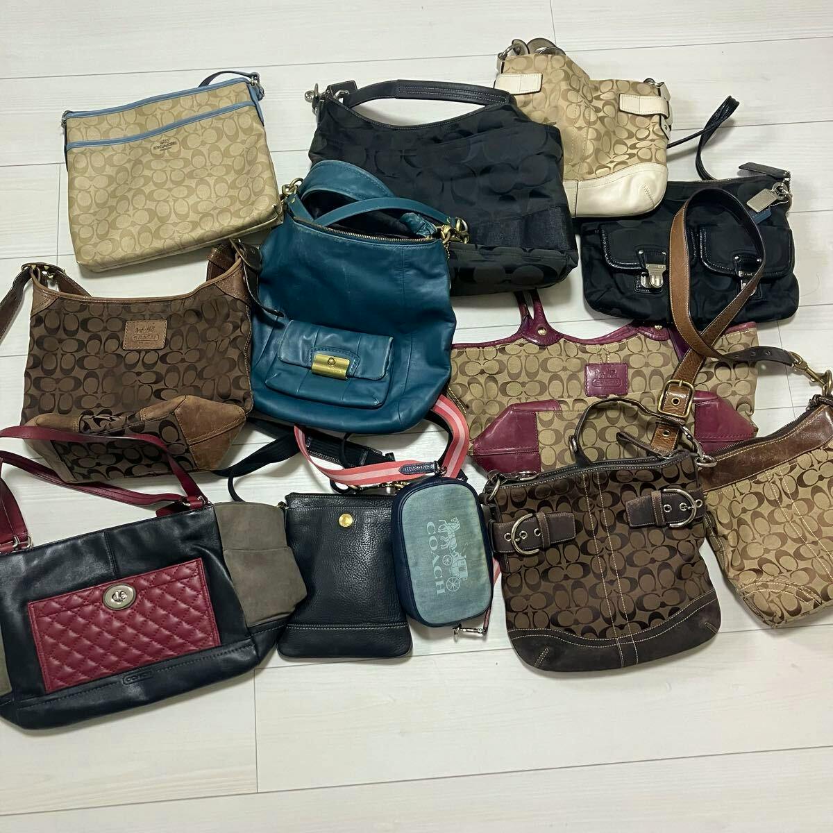A collection of COACH bags in signature C pattern and various colors arranged on a light-colored floor.