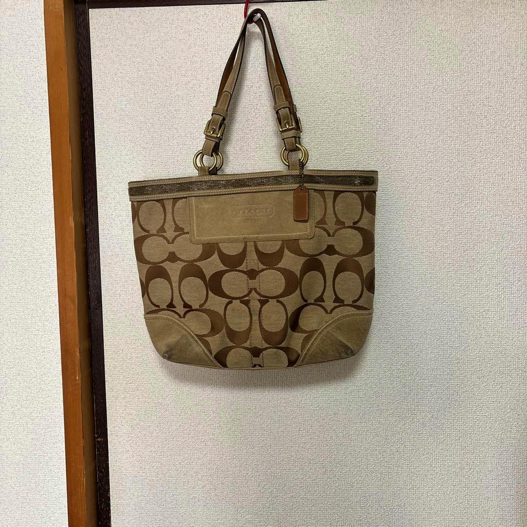 Brown COACH signature canvas tote bag with double shoulder straps hanging on a wall.