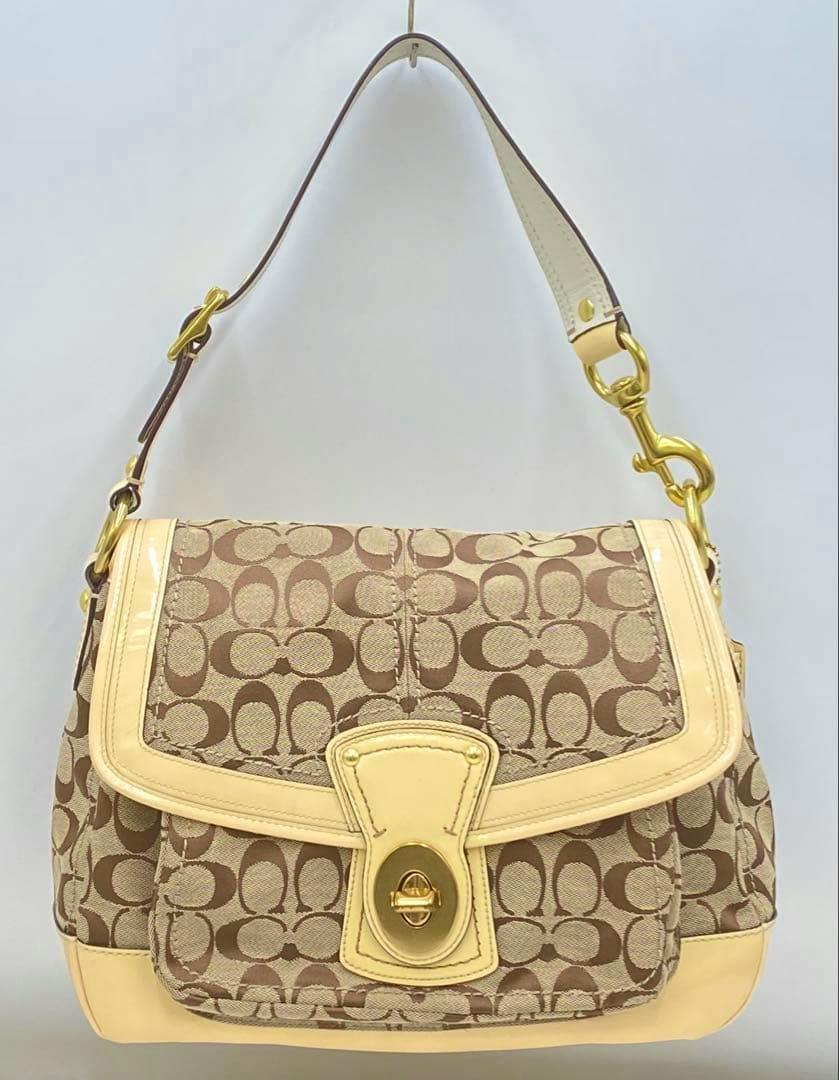 Front view of a COACH signature shoulder bag in beige monogram canvas with pale leather trim and a gold turn-lock closure.