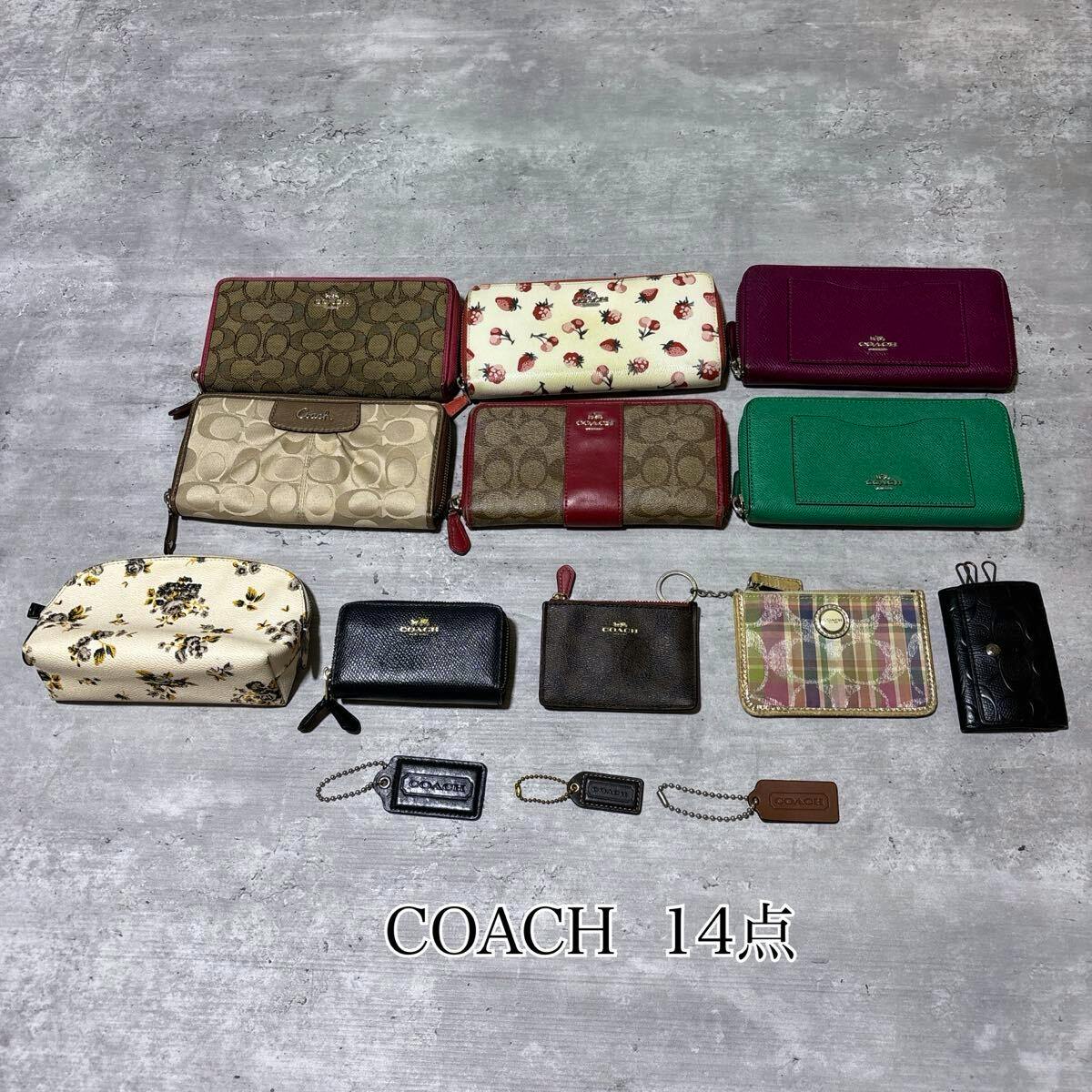 Fourteen COACH wallets and small accessories (wallets, coin cases, pouches, keycases, and charms) arranged on a gray surface.