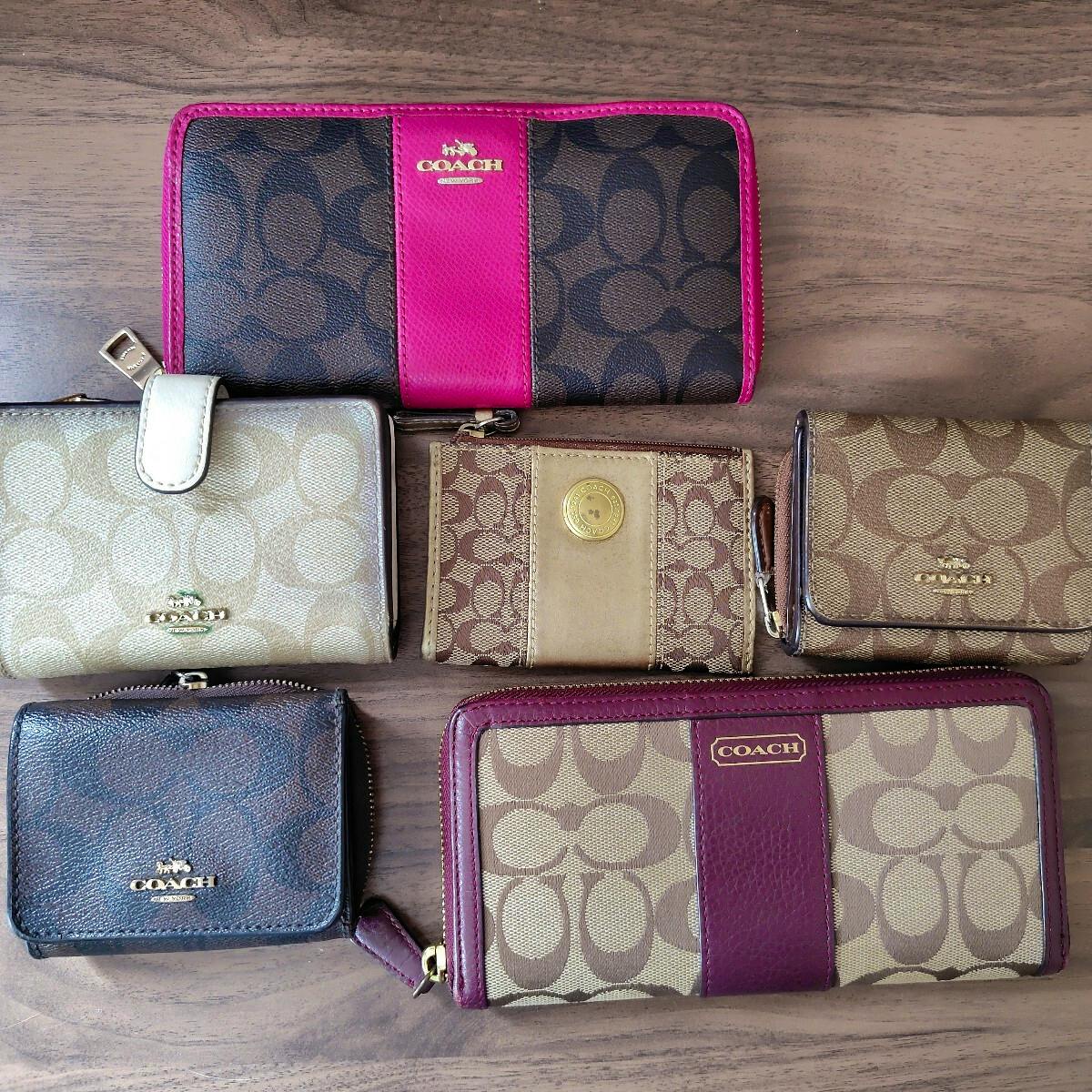 Six COACH wallets and small coin purses arranged on a wooden surface showing signature canvas patterns and leather trim.