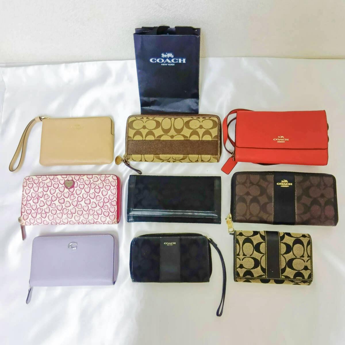 Nine Coach wallets and a small Coach shopping bag displayed on a white surface.