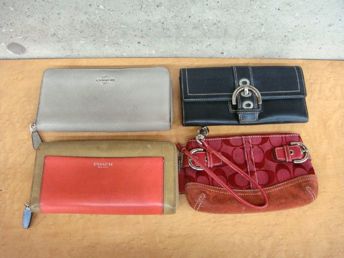 Four Coach wallets and pouches laid flat: a grey zip-around wallet, a black flap wallet, a red-and-tan zip wallet with COACH logo, and a red signature wristlet.