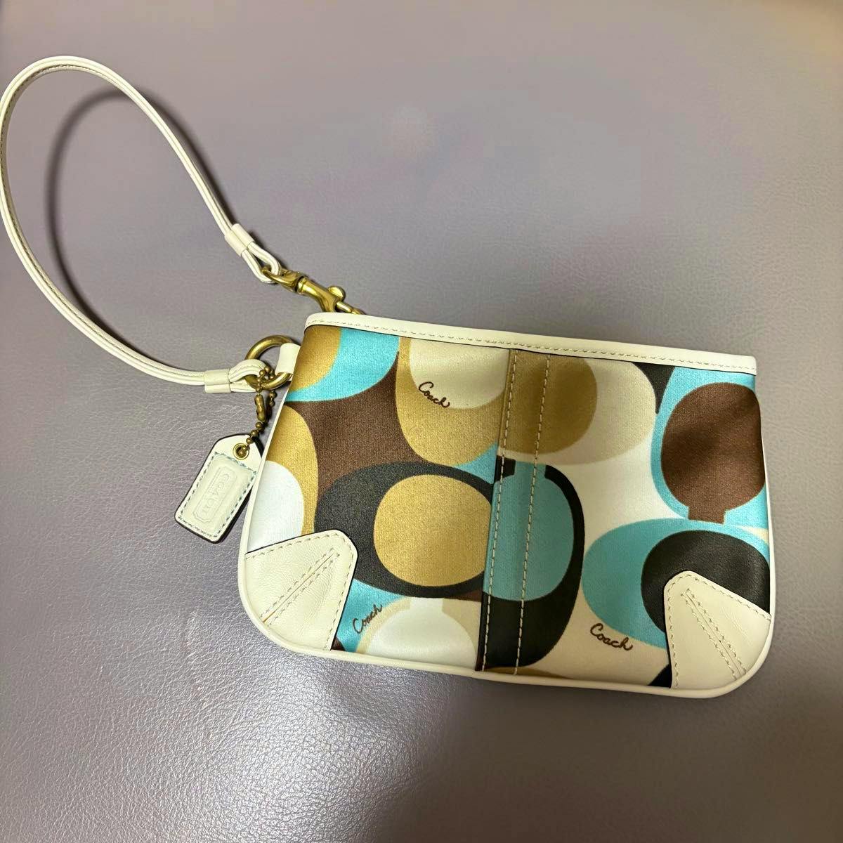 Coach wristlet pouch in multicolor signature canvas with white leather trim, white wrist strap, and a Coach hang tag.