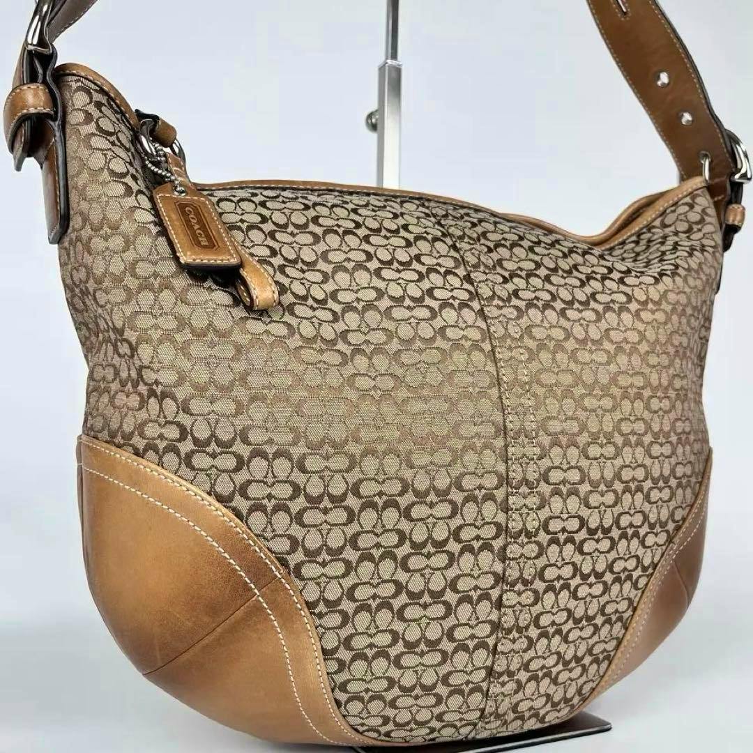 Beige Coach signature canvas half-moon one-shoulder bag with tan leather trim and a Coach hang tag visible.
