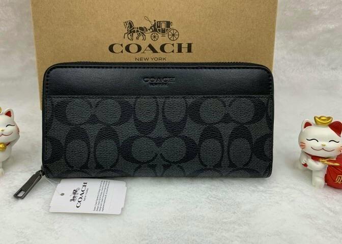 Front view of a COACH long zip-around signature cow leather wallet with its tag and box behind it.