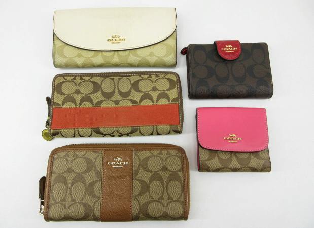 Five COACH wallets in signature canvas and leather arranged on a white background.