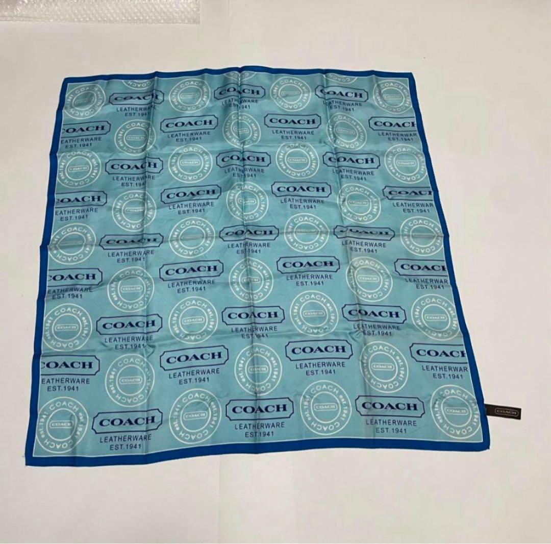 Light blue silk handkerchief printed with repeating COACH logos and circular emblems on a white background.