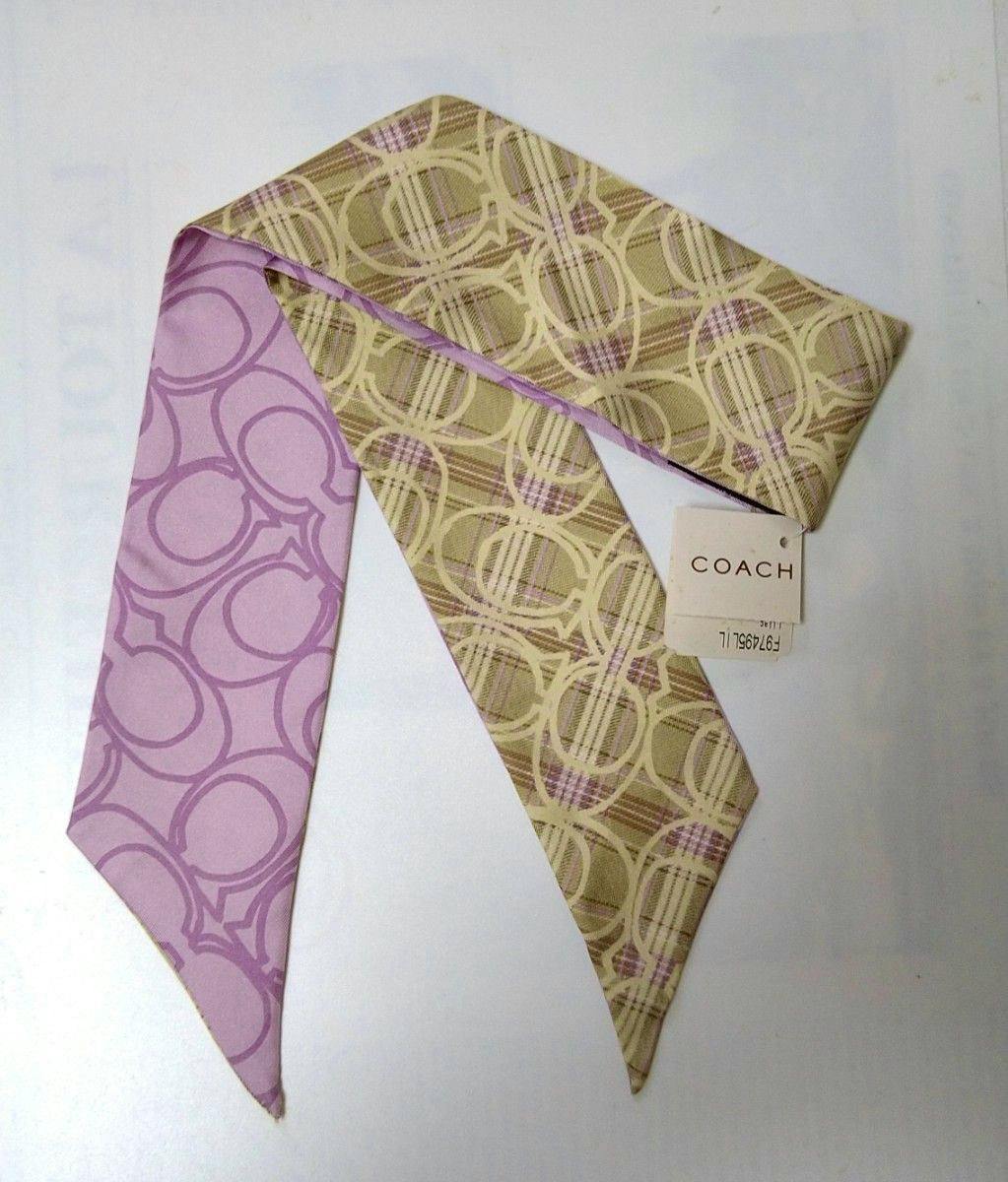 A Coach silk ribbon scarf laid flat showing lilac and beige patterned sides and an attached Coach tag.