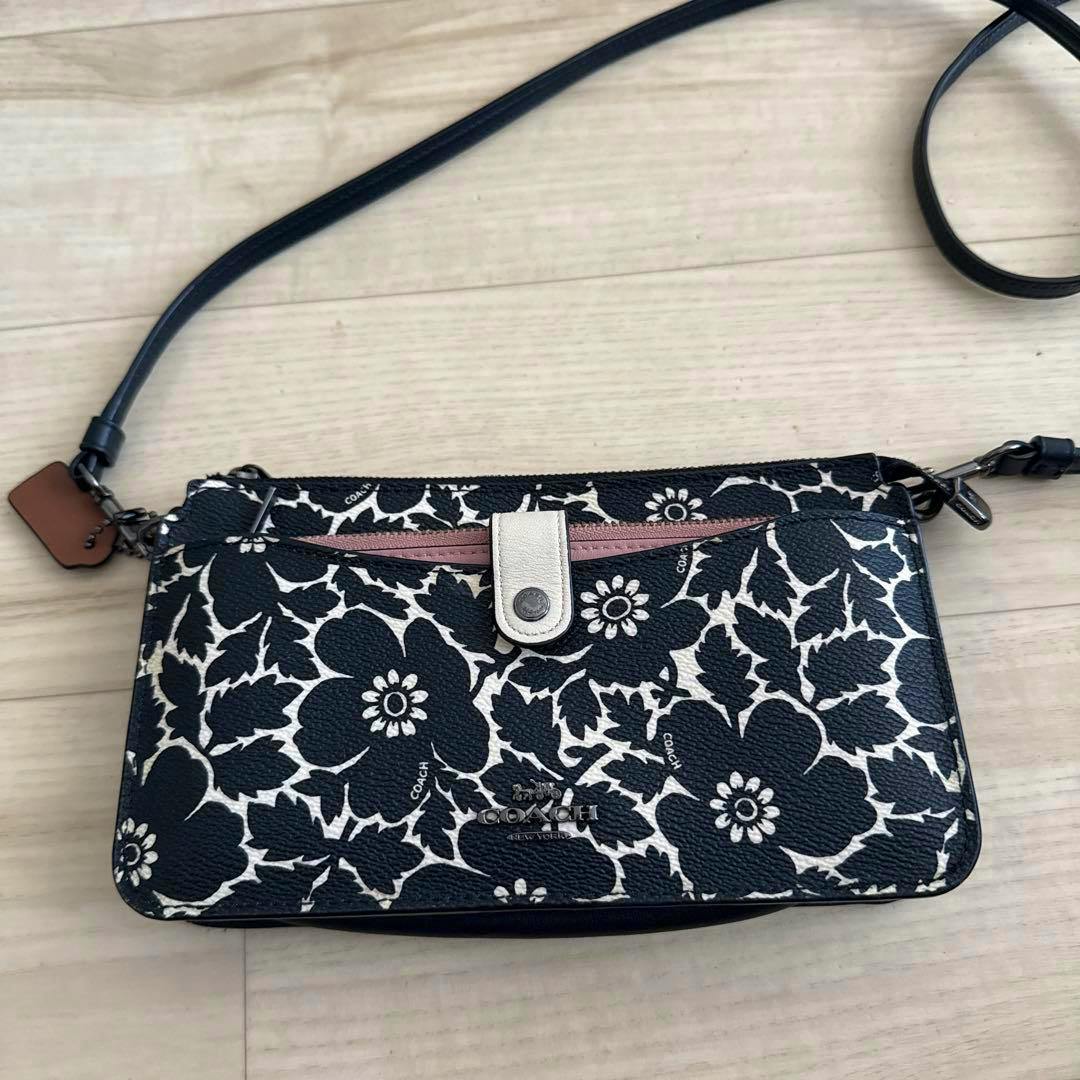 A COACH slim crossbody/wristlet bag in black and white floral print with strap on a light wood floor.