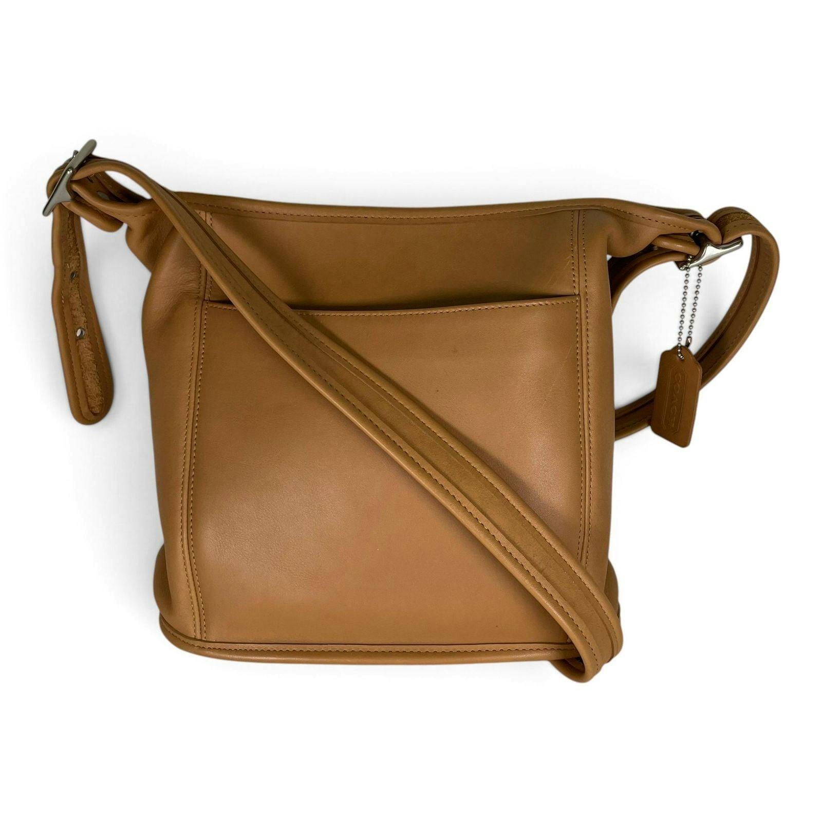 Tan leather Coach shoulder bag front view with crossed strap and a Coach hang tag visible.