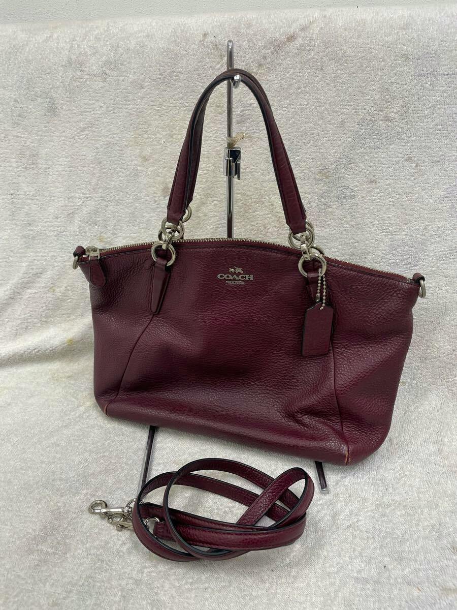 Front view of the COACH small Kelsey shoulder handbag with top handles and a detachable shoulder strap displayed on a stand.