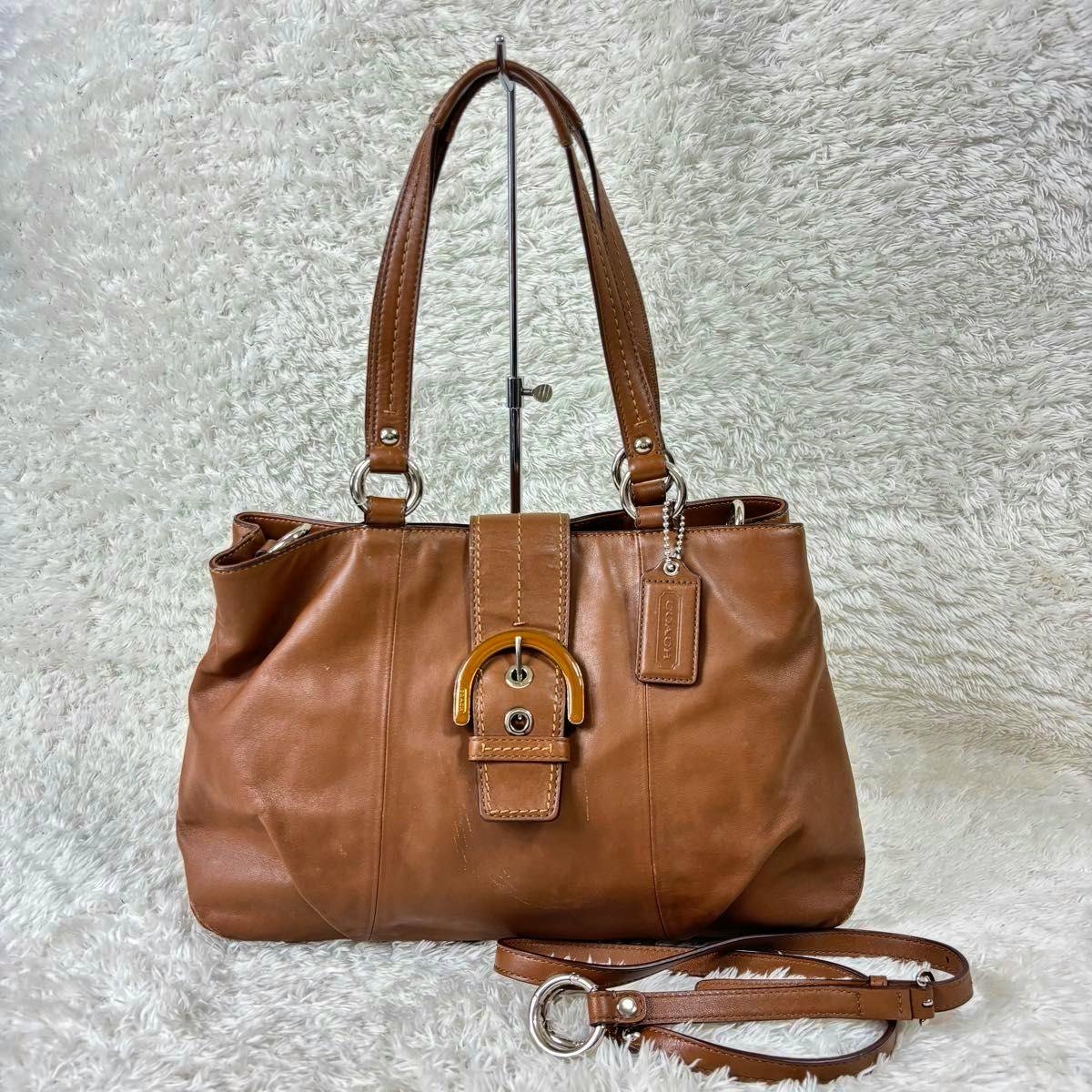 Brown COACH Soho 2-way leather shoulder and handbag with front buckle and detached strap on a light textured background.