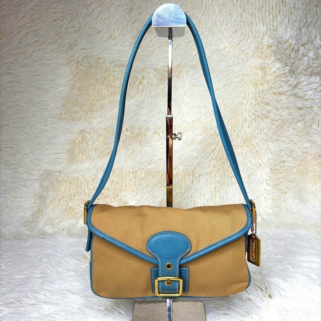 COACH SOHO Canvas Blue one-shoulder bag displayed hanging on a stand, showing tan canvas body with blue leather trim and gold hardware.