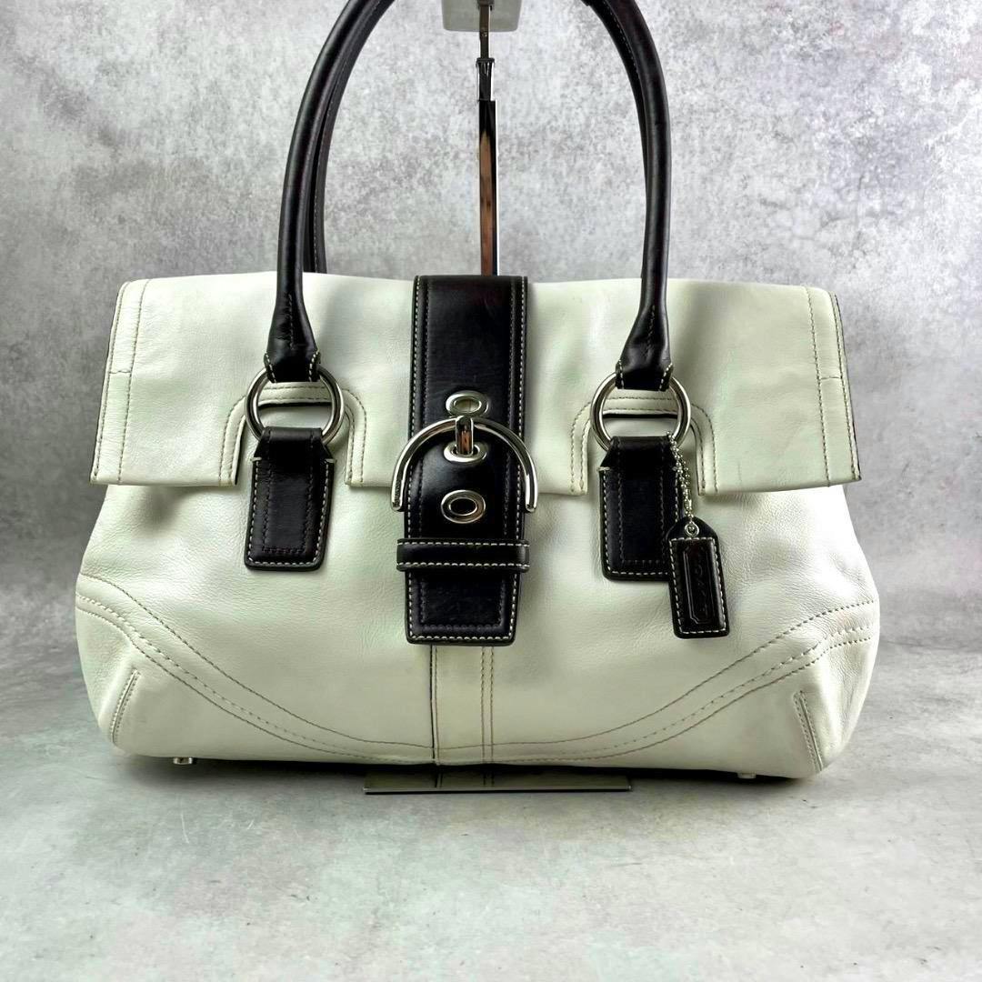 Front view of the Coach Soho hand bag in white leather with black handles, a black center buckle strap, and silver hardware.