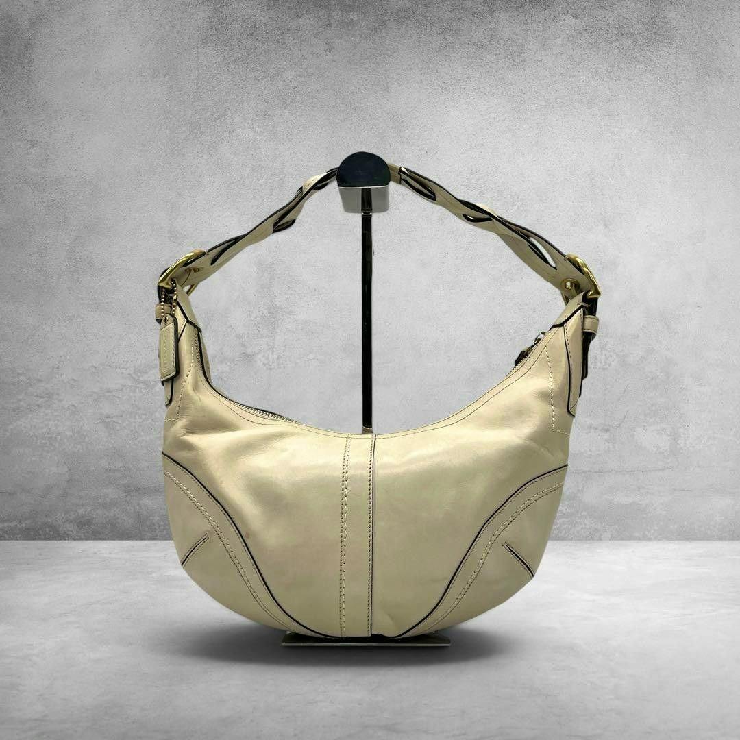 Cream leather COACH Soho Hobo crescent bag displayed on a stand, front view showing the strap and crescent shape.