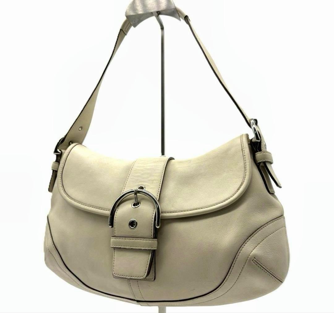 Cream leather Coach Soho hobo flap handbag with front buckle shown against a white background.