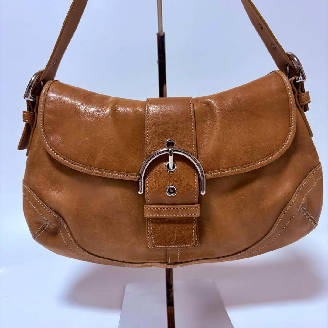 Front view of a tan cow leather Coach Soho hobo one-shoulder bag showing its buckle closure and shoulder strap.