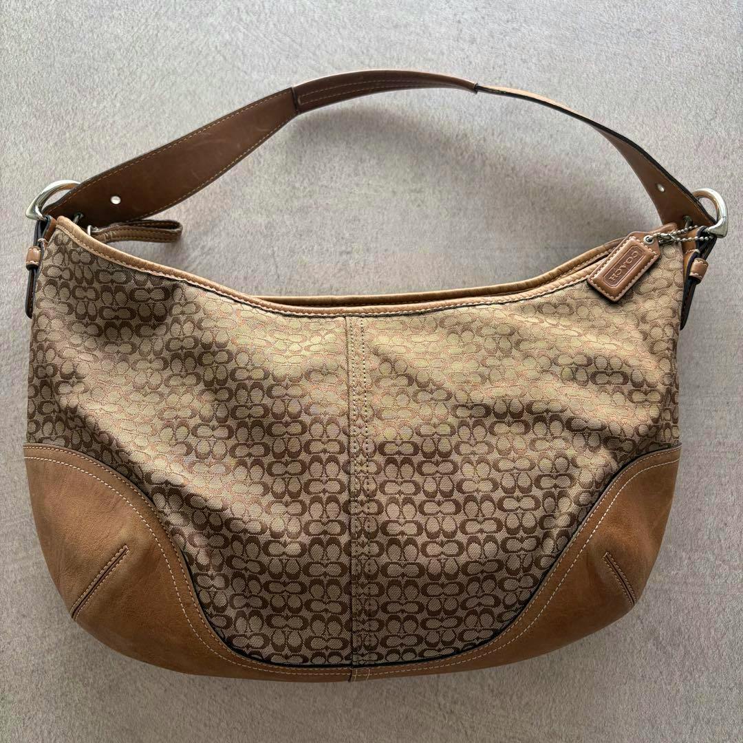 Front view of a Coach Soho hobo one-shoulder bag in brown signature canvas with tan leather trim and a Coach hang tag.