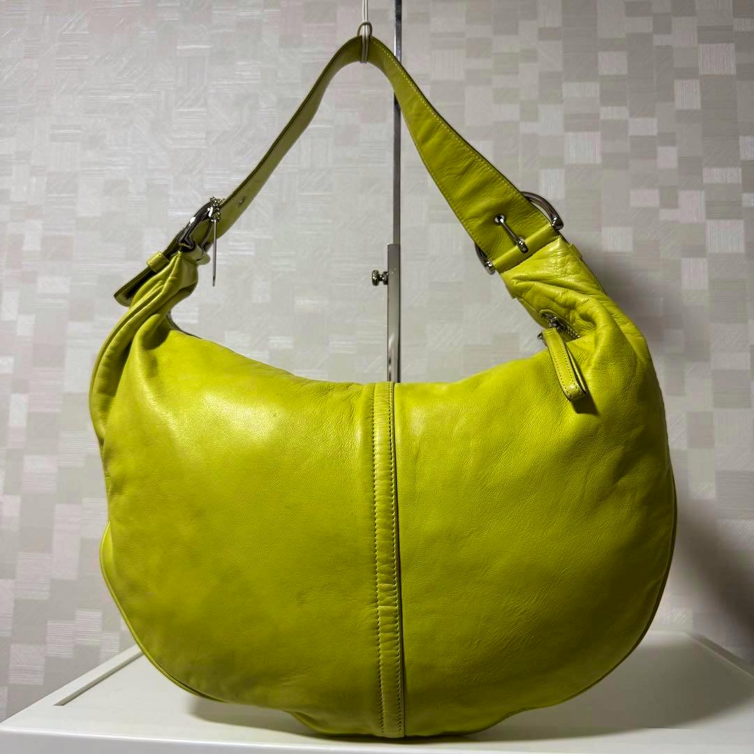 Front view of a lime green Coach leather hobo shoulder bag hanging on a metal stand.