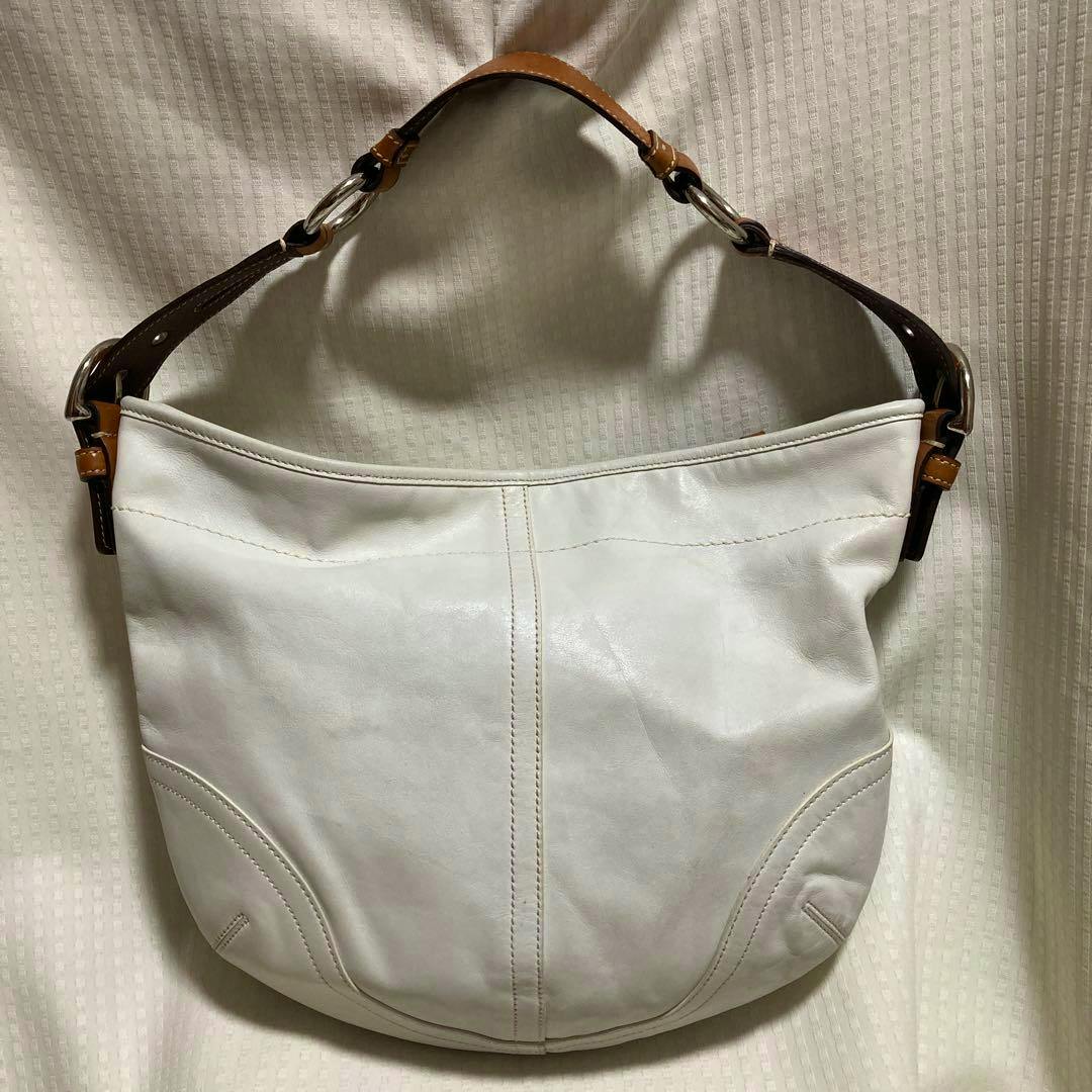 White leather COACH Soho shoulder bag with brown leather strap and silver hardware against a light fabric background.