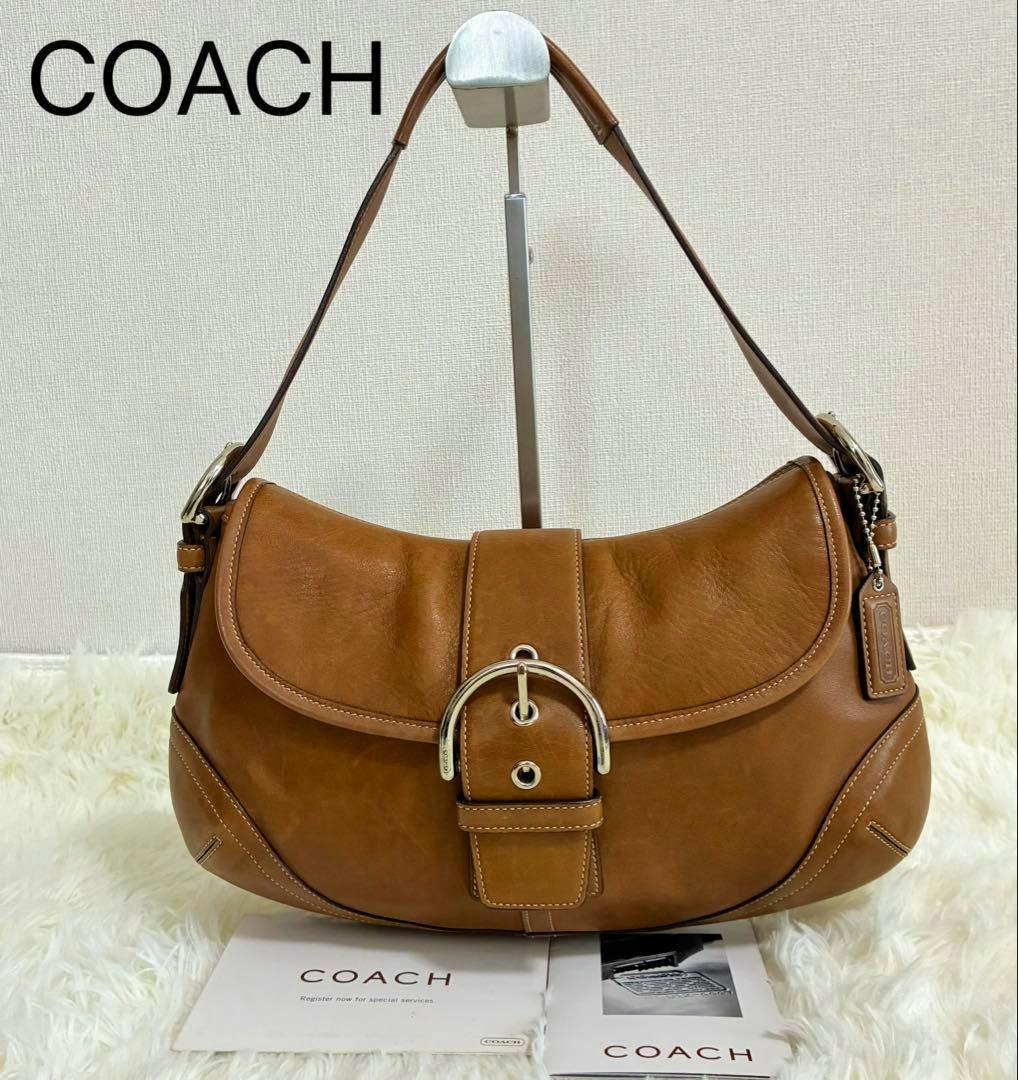 Brown COACH Soho cow leather shoulder bag on a display stand showing the front buckle detail.