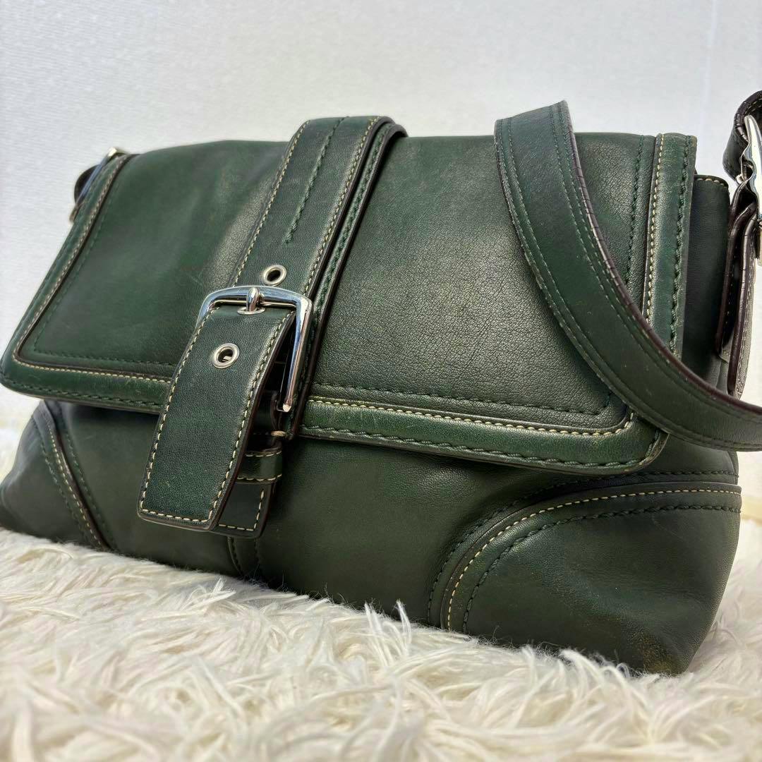Close-up of the dark green leather shoulder bag front flap showing the buckle and strap.