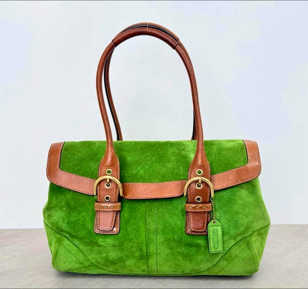 Front view of a green Coach SOHO shoulder bag with brown leather handles, brass buckles, and a green hang tag.