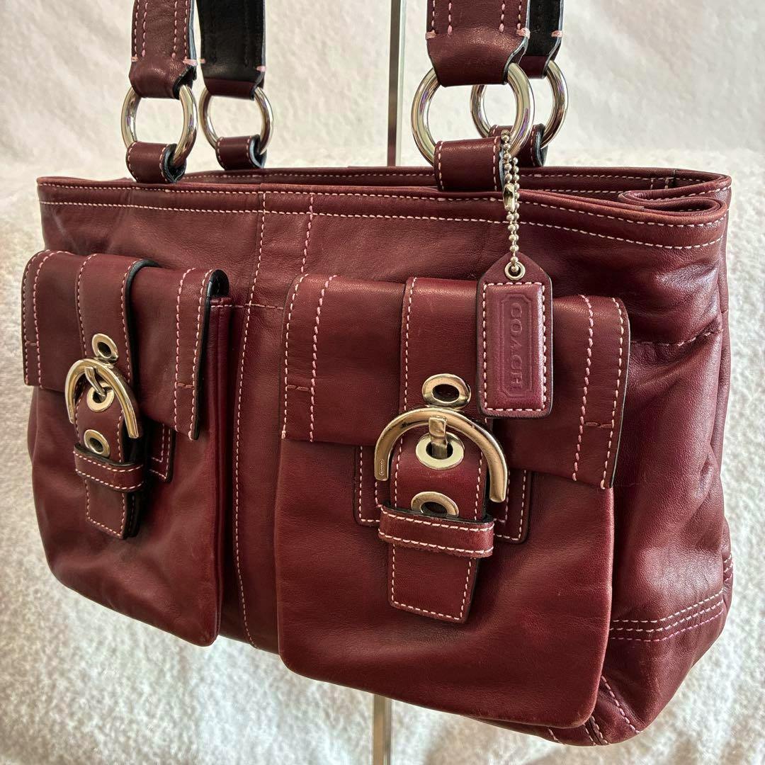 Bordeaux Coach Soho cow leather tote bag with two front buckle pockets and double shoulder straps on a light background.