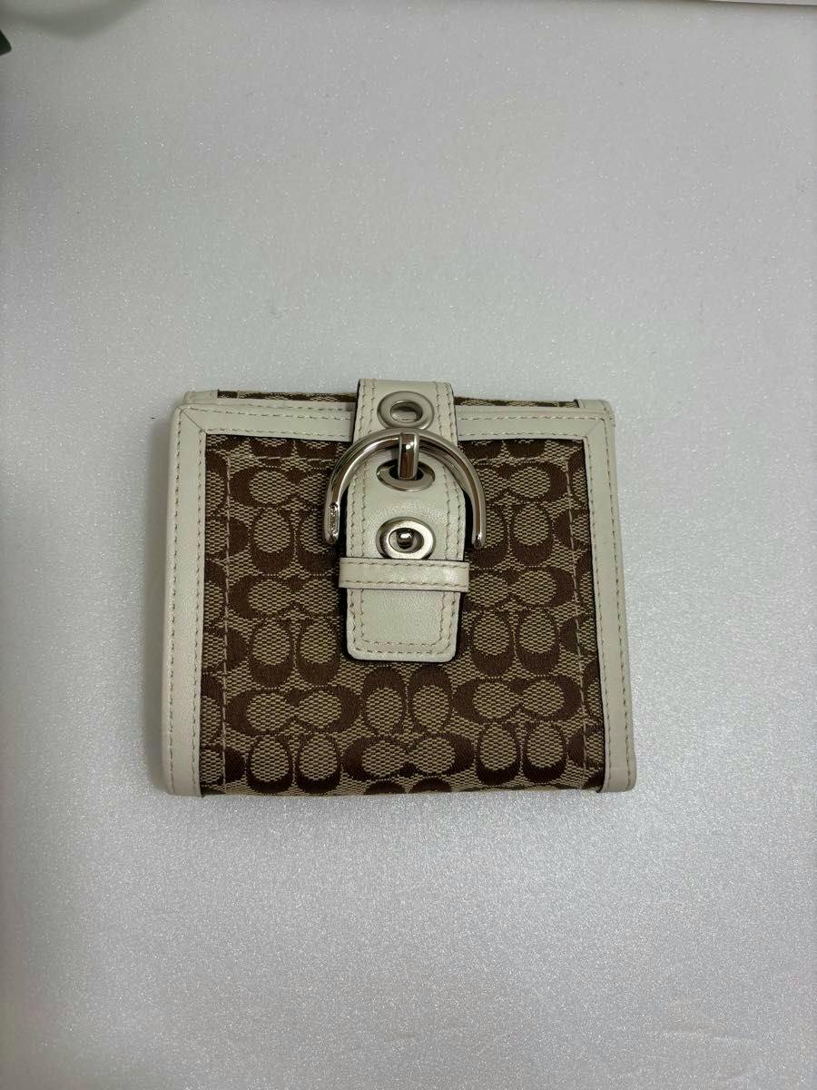 Front view of a COACH Soho mini signature bi-fold wallet in brown canvas with white trim and a silver-tone buckle closure.
