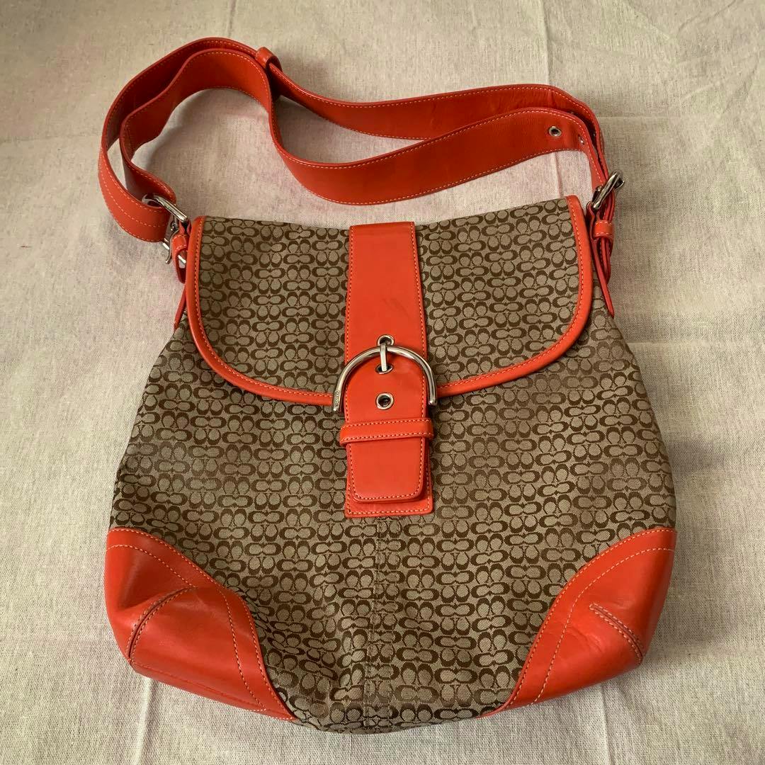 COACH Soho mini signature canvas shoulder bag in brown monogram with orange leather trim and buckle, shown laying flat.