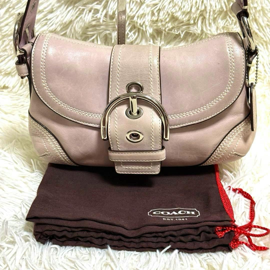 Front view of the pink Coach Soho one-shoulder cow leather bag with buckle detail on a Coach dust bag.