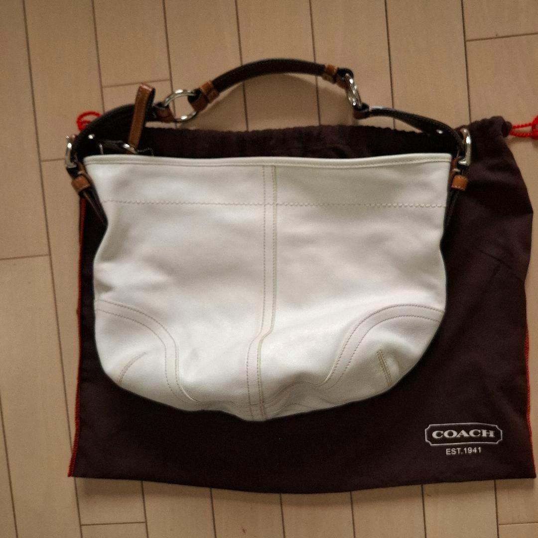 White COACH Soho one-shoulder leather bag laid flat on a brown COACH dust bag.