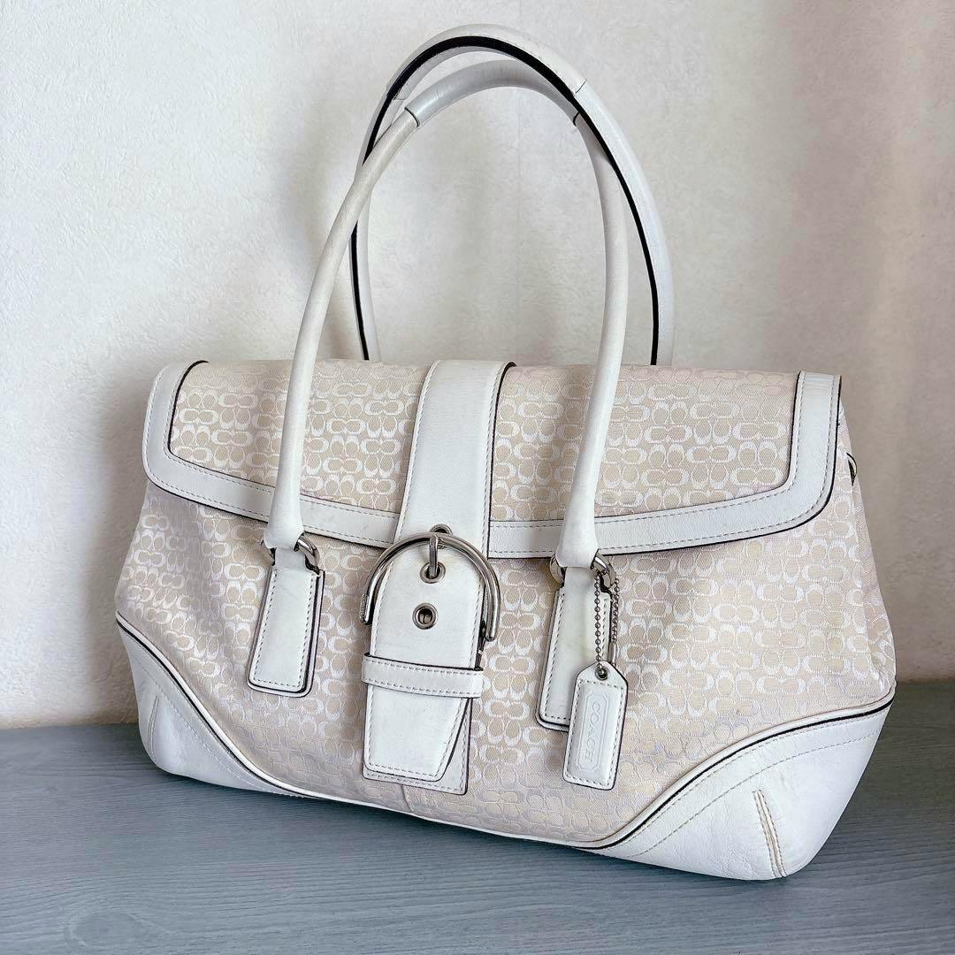 Front-angle photo of the COACH Soho Signature Flap Hand Bag (cow leather) showing the bag's flap, buckle detail, and double top handles on a neutral background.