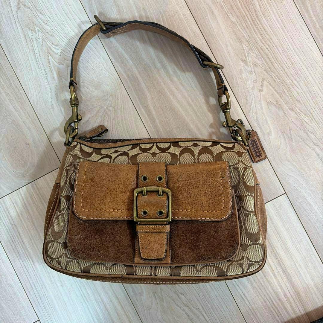 Front view of the Coach one-shoulder canvas bag with signature print, brown leather front pocket, buckle, and shoulder strap.