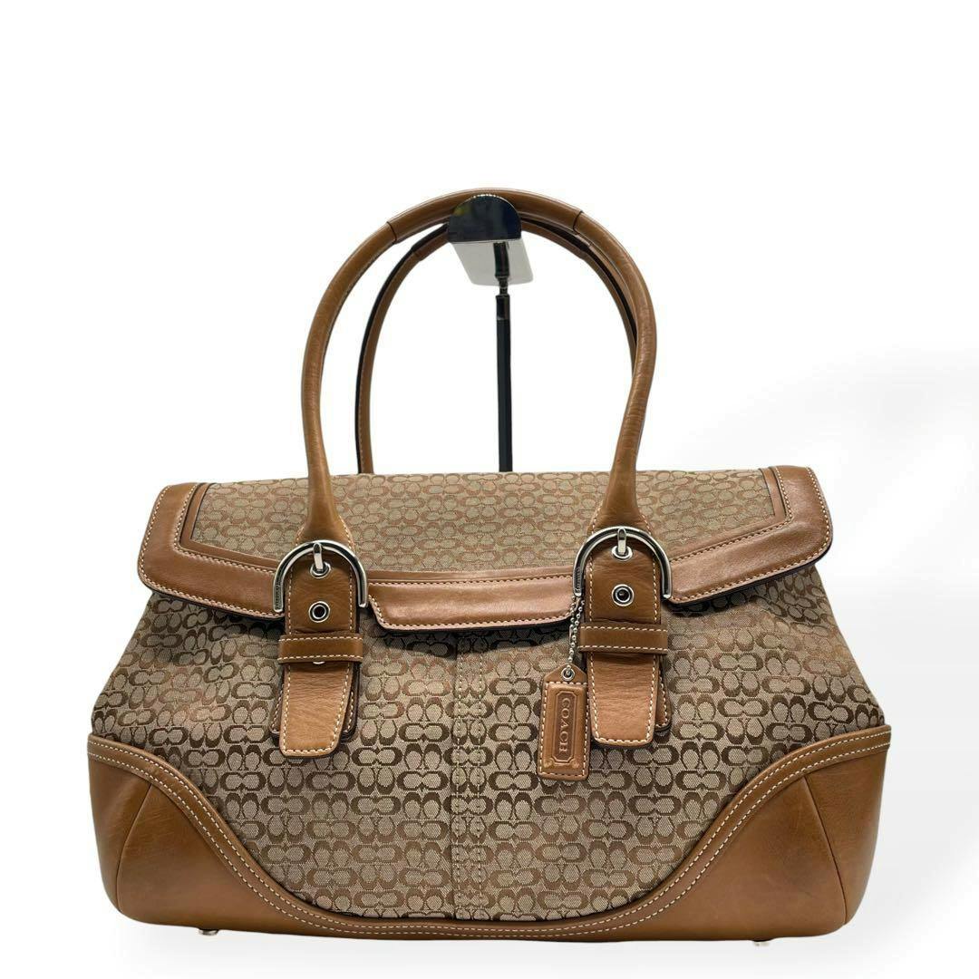 Front view of a brown Coach Soho signature tote bag with leather trim, dual handles, and a Coach hang tag.