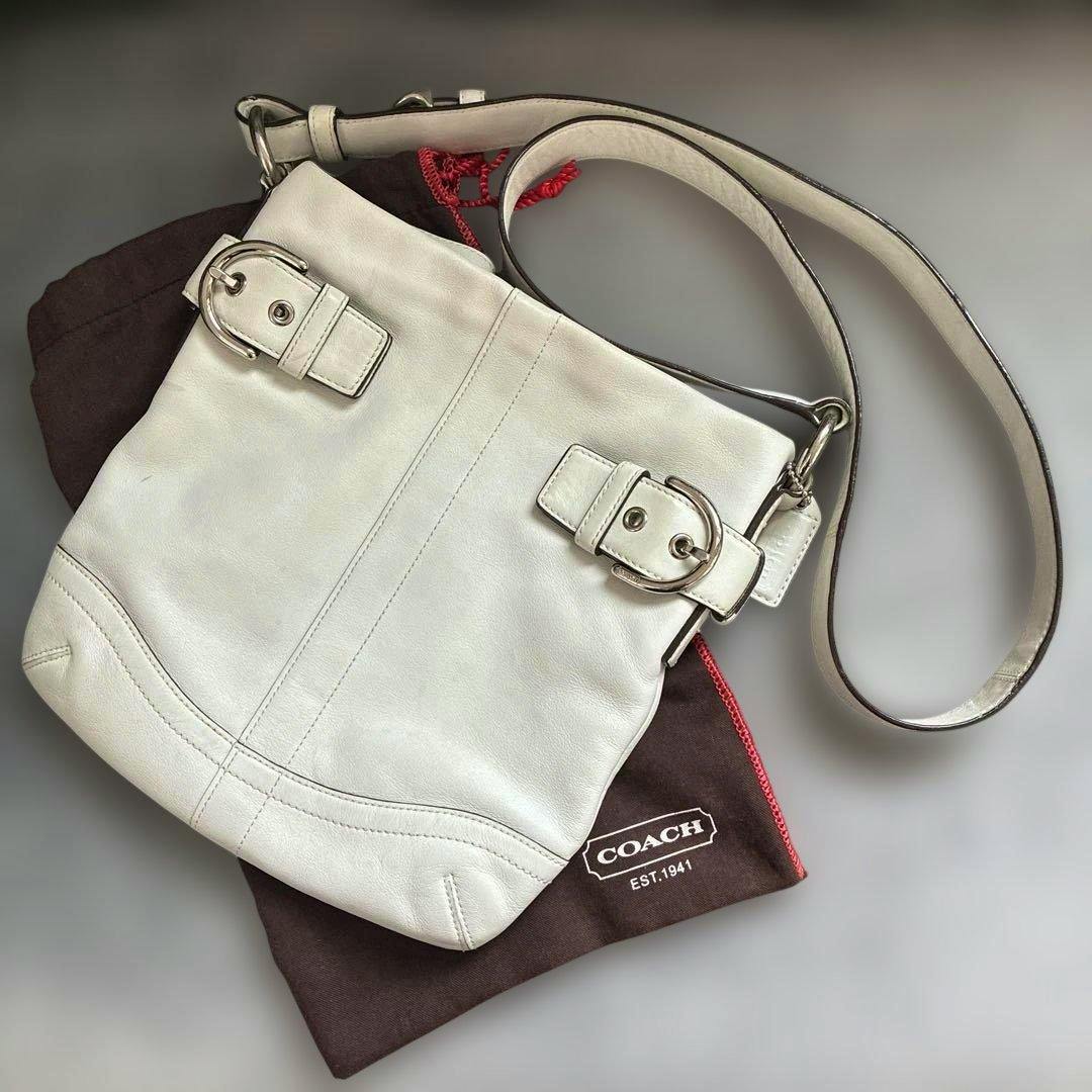 White COACH Soho Slim Duffle shoulder bag in cow leather pictured on top of a brown COACH dust bag.