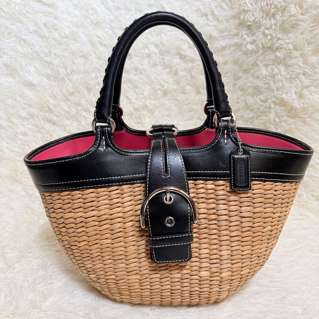 Coach Soho straw basket bag with black leather trim, buckle strap, and red interior on a light background.
