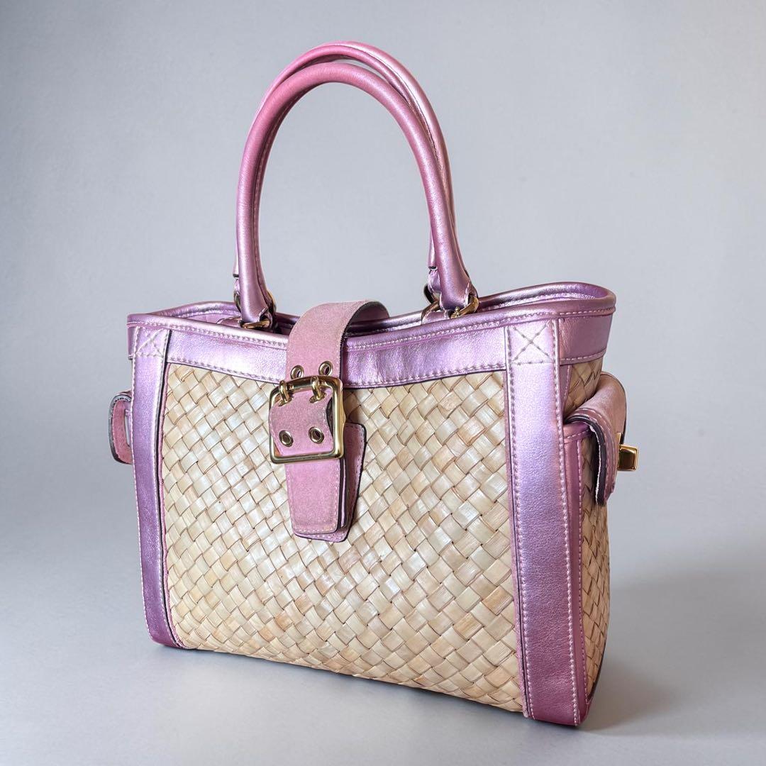 Woven basket bag with pink leather trim, top handles, and a front turn-lock strap photographed against a neutral background.