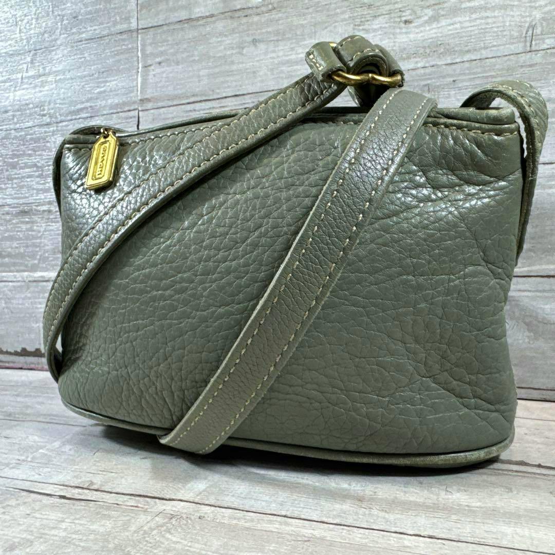Green COACH leather shoulder bag shown from the side with its shoulder strap and a gold COACH tag.
