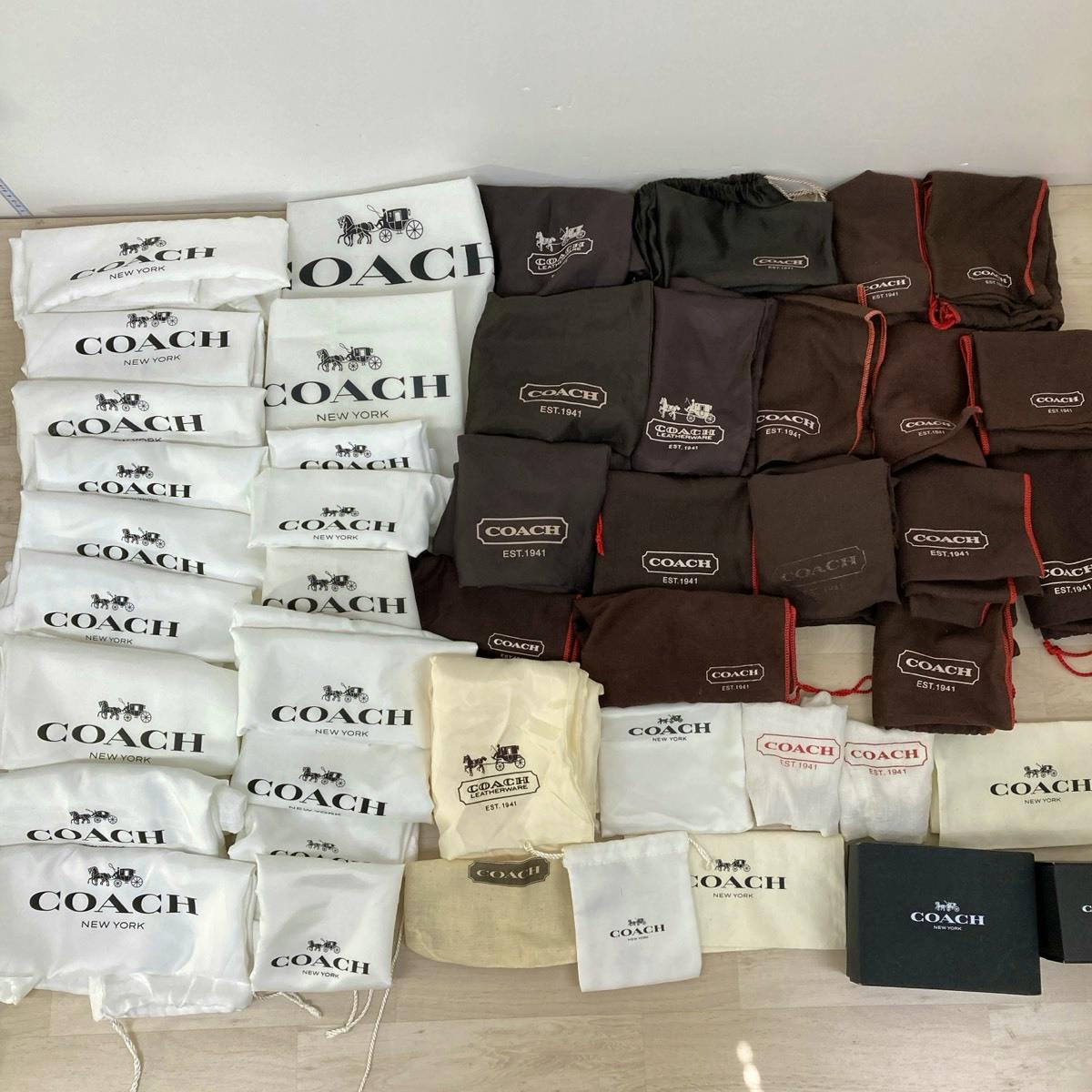 Multiple COACH branded white and brown dust bags and black COACH boxes arranged on a floor.