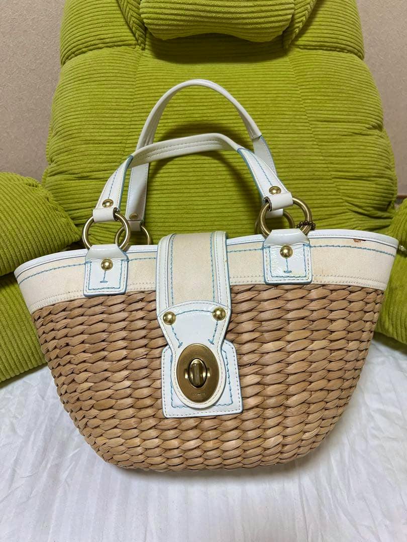 Front view of a COACH straw basket bag with white leather trim and a turnlock closure.