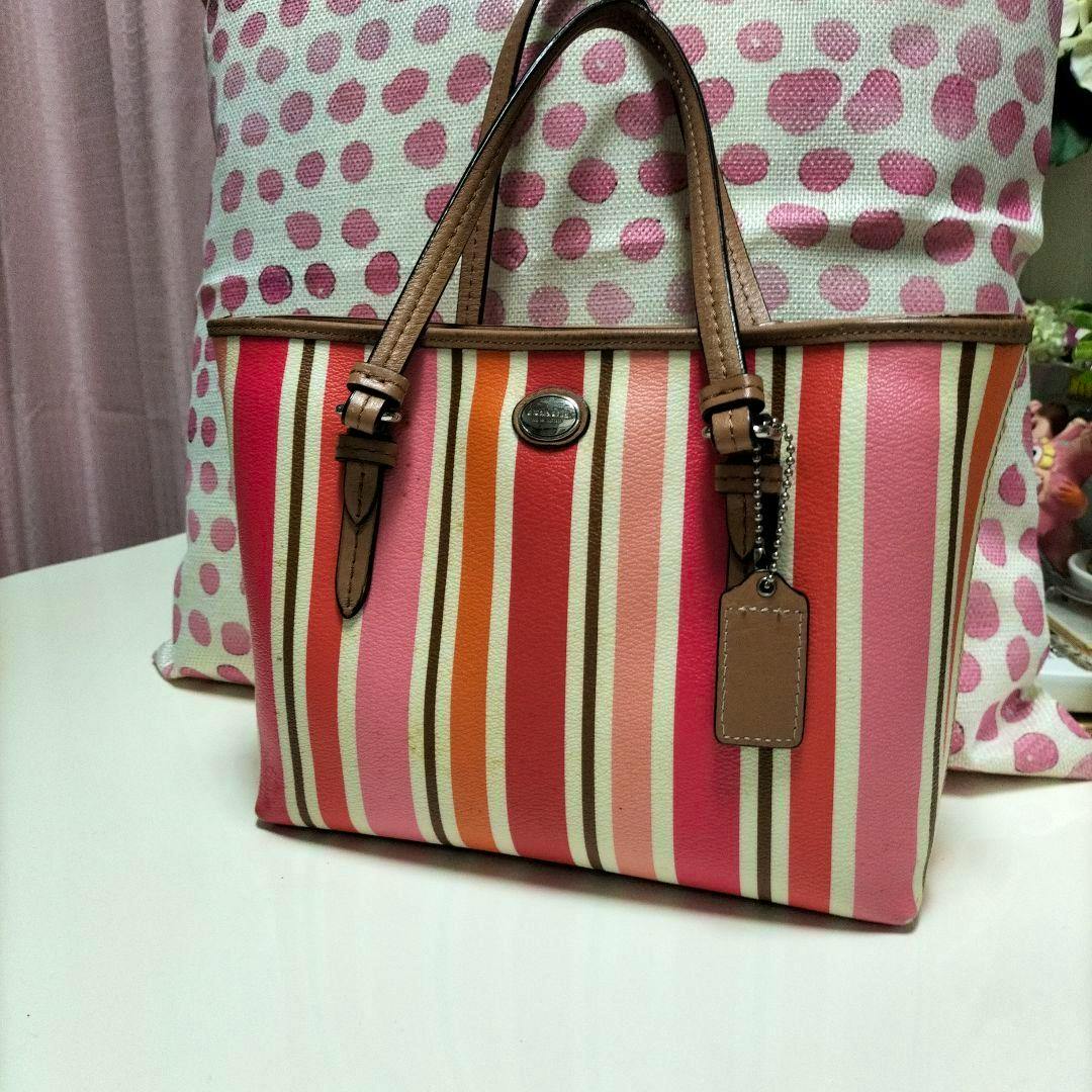 Front view of the Coach striped canvas tote bag with pink, red, orange and white vertical stripes, brown leather handles, and a leather hang tag.