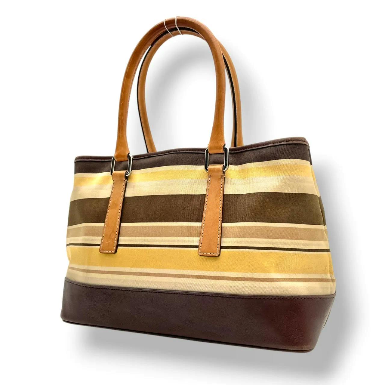 Front view of a COACH striped canvas and leather tote bag in brown, beige, and yellow with leather handles.