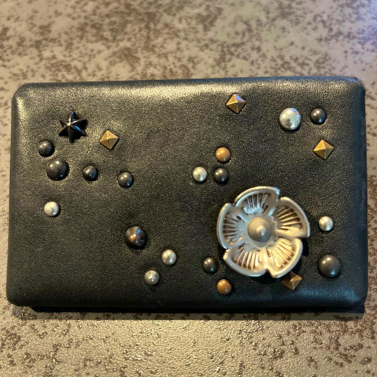 Black Coach leather card case front with assorted stud embellishments and a metal flower motif.