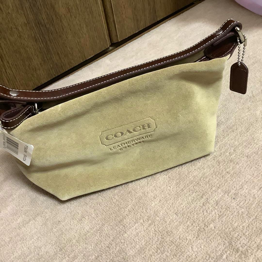 Brown suede COACH accessory pouch handbag with a brown leather strap and embossed COACH logo on a carpeted floor.