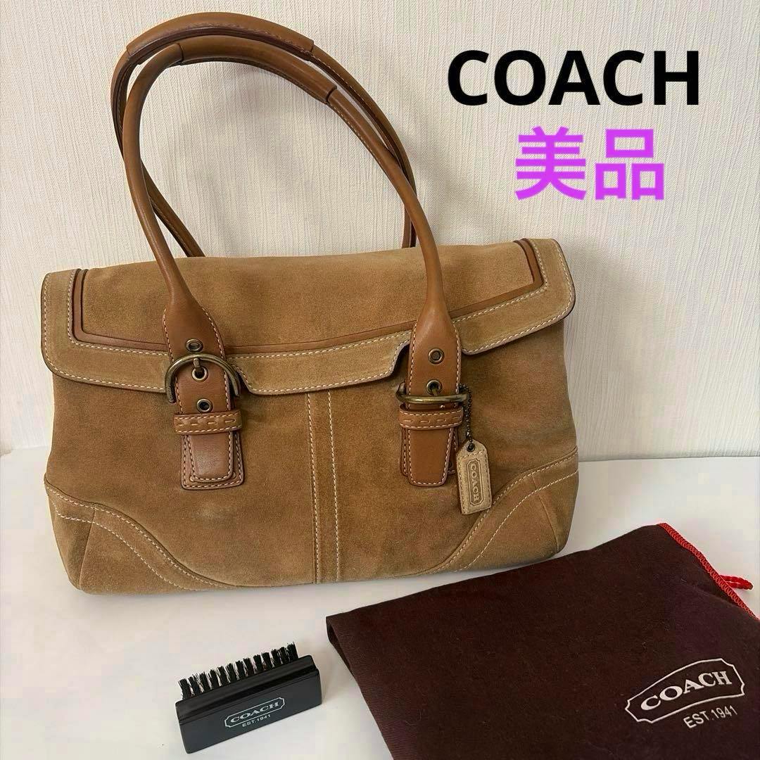 Beige Coach suede and leather tote handbag with double handles and a Coach hang tag, shown with a small brush and a Coach dust bag.