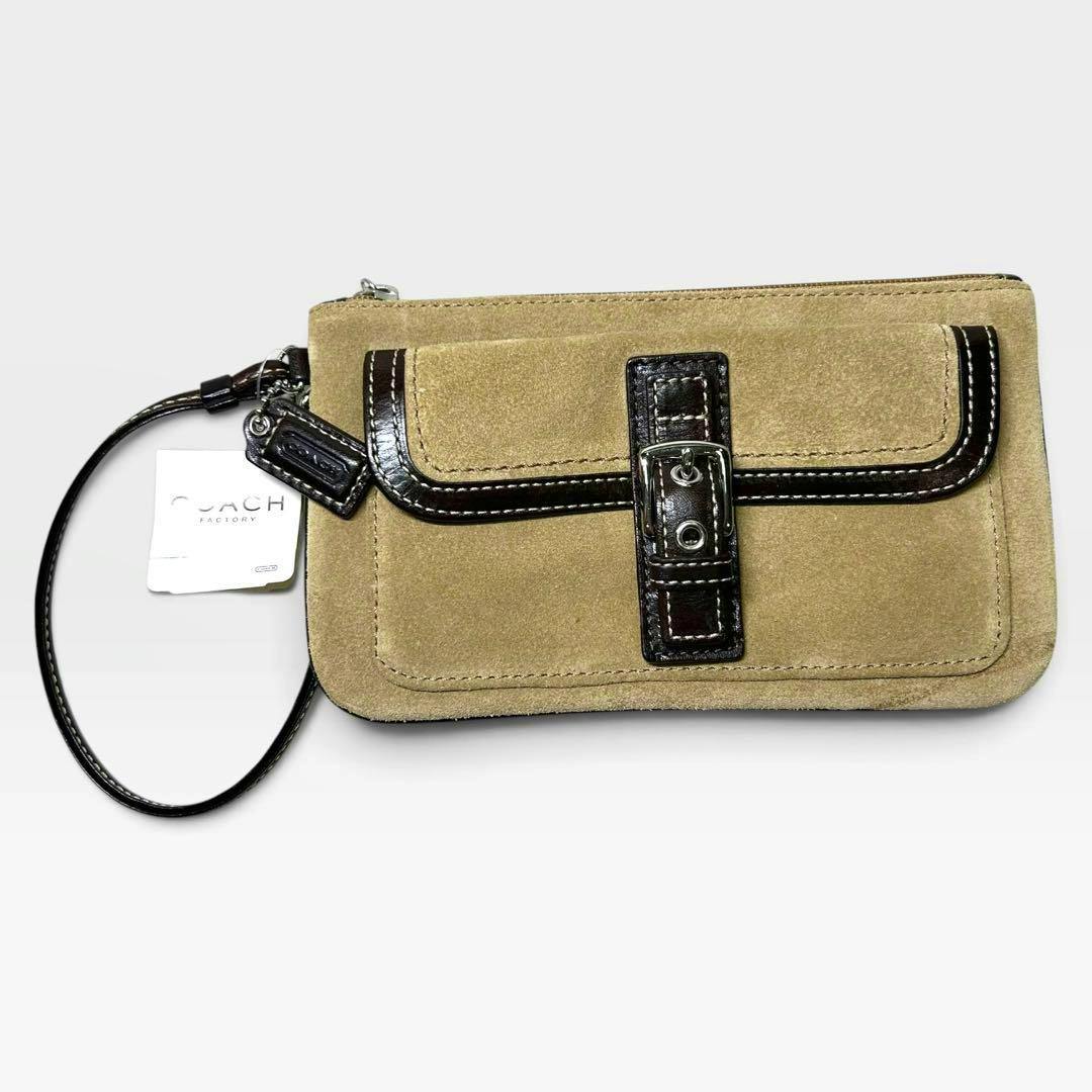 Beige suede COACH wristlet pouch with dark leather trim, front buckle detail, and wrist strap on a plain white background.