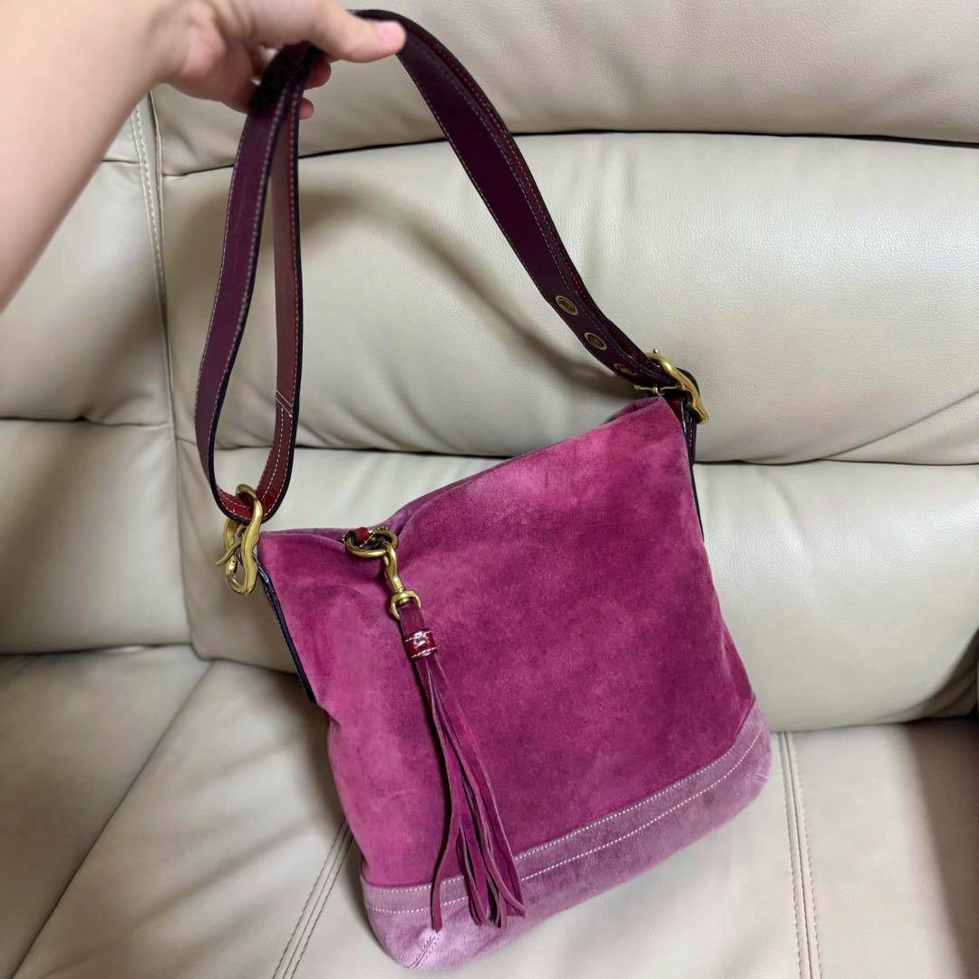 Purple suede COACH hobo shoulder bag with a leather strap and tassel detail shown on a light-colored sofa.