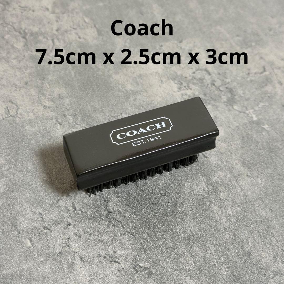 Black Coach shoe-care cleaning brush with COACH logo on top photographed on a gray surface with dimension text visible.
